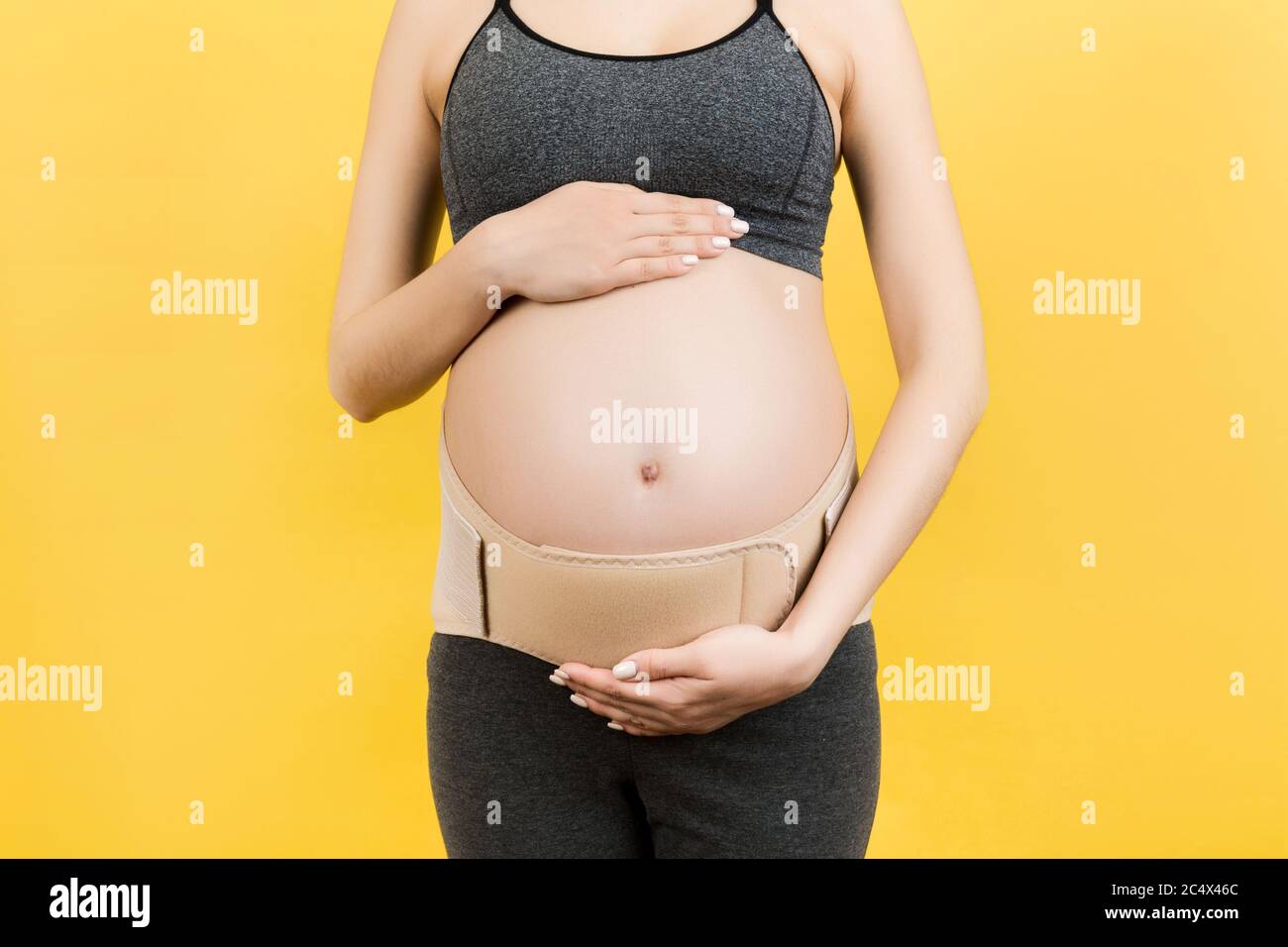 Gros plan de la femme enceinte dans un bandage de grossesse élastique pour faire disparaître la douleur sur fond jaune avec l'espace de copie. Support abdominal orthopédique être Banque D'Images