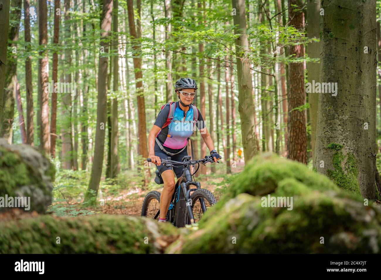 Jolie femme âgée en train de se rendre sur son vélo électrique de montagne sur un sentier de forêt rocheuse en Suisse franconienne, en Bavière, en Allemagne Banque D'Images