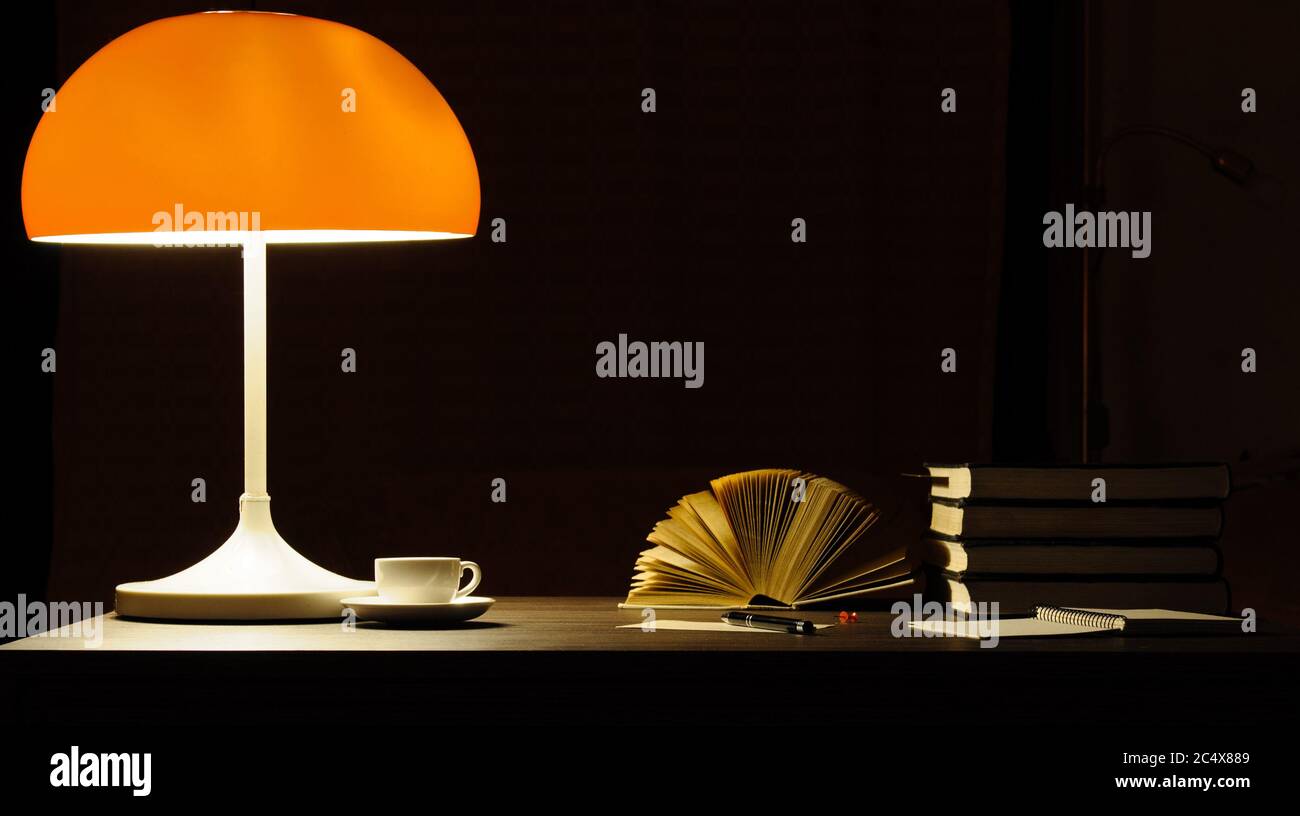 Une lampe de table avec abat-jour orange illumine les livres sur le bureau Banque D'Images