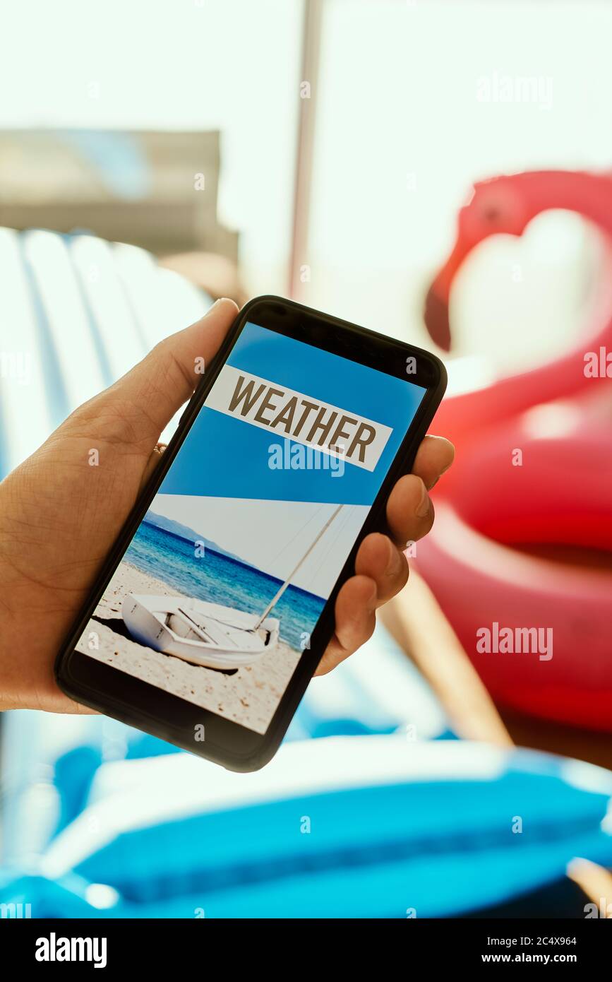 gros plan d'un jeune homme, portant des vêtements d'été décontractés, assis sur un fauteuil, ayant son smartphone dans les mains avec le texte météo dans son écran, Banque D'Images