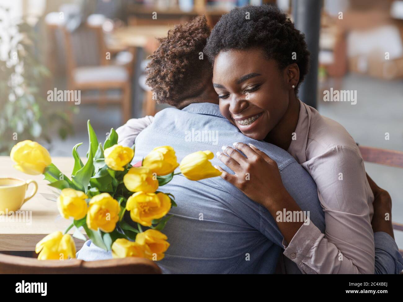 Fille noire embrassant son petit ami et tenant un bouquet de tulipes jaunes au café Banque D'Images