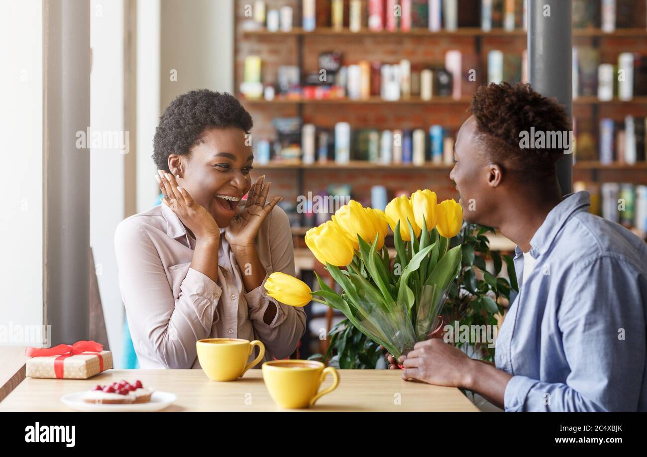 Un sympathique gars afro-américain exprimant son amour à sa petite amie, présentant ses fleurs au café Banque D'Images