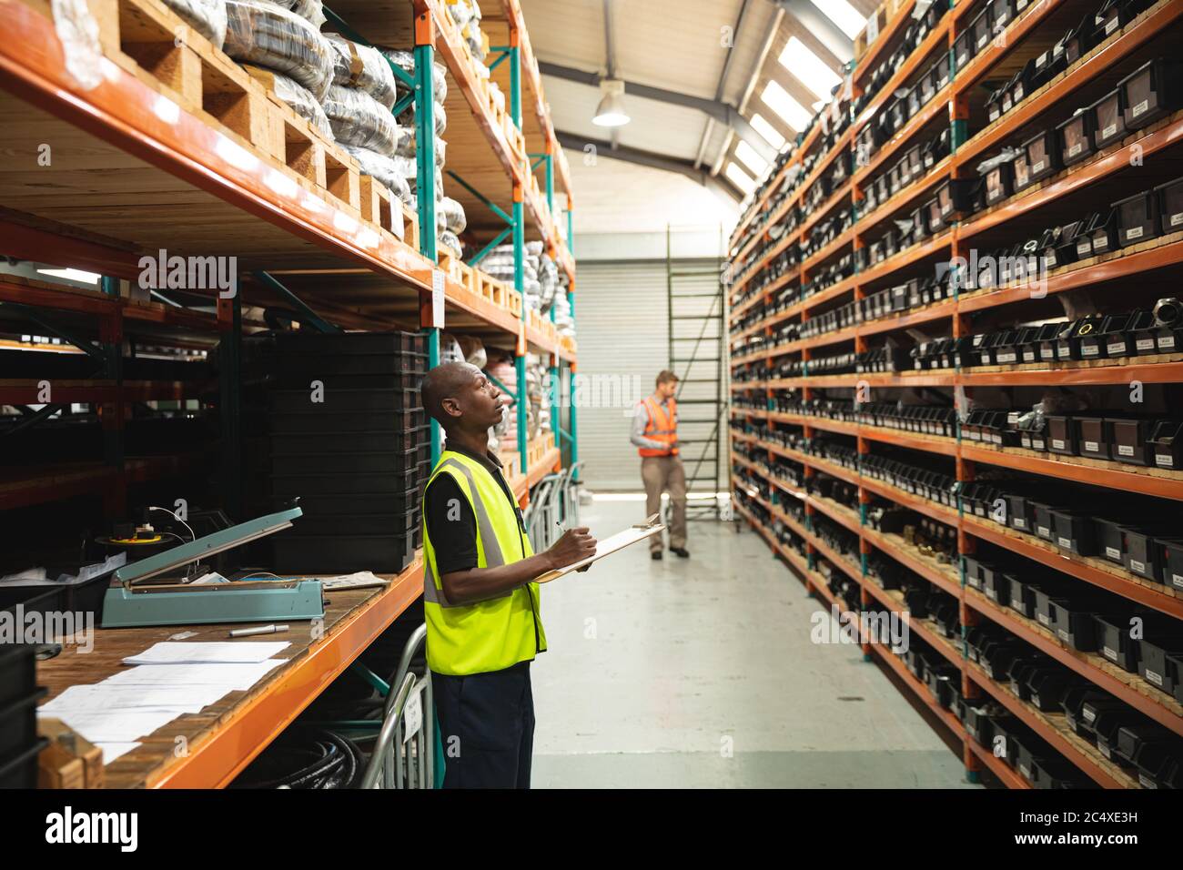 Un ouvrier de l'usine portant un gilet Hi-vis tenant une pince et vérifiant le stock à l'usine Banque D'Images