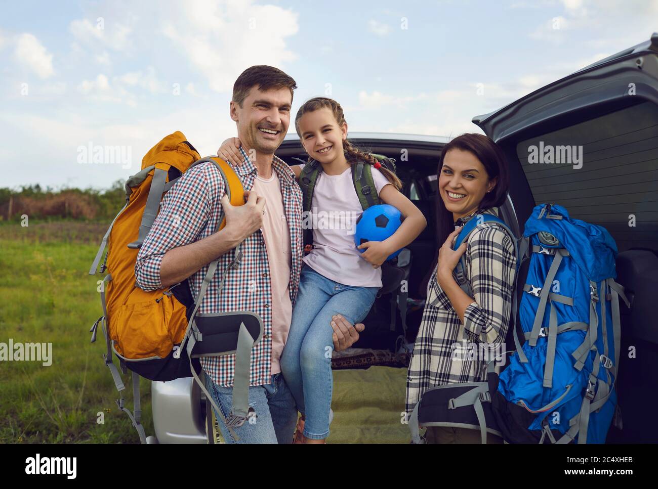 Famille souriante de voyageurs en voiture debout dans la nature en été. Banque D'Images