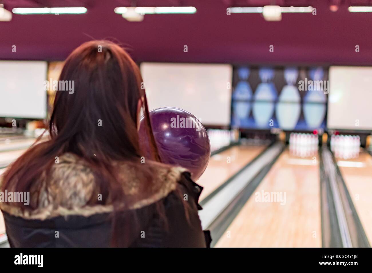 Un bowling tout en étant visé à la cible par une femme adulte dans un tournoi de bowling. Boule de bowling violette et arrière-plan de piste de bowling floue Banque D'Images