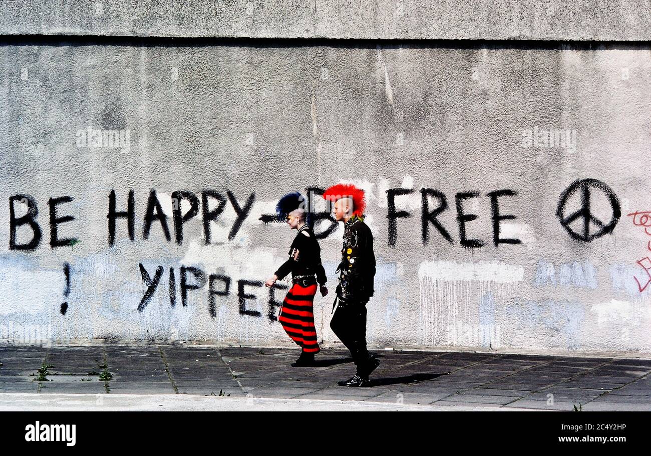 La scène de rue d'un couple d'adolescents punk rock marchant a passé un slogan CND graffiti. Londres Angleterre Royaume-Uni. Vers les années 1980 Banque D'Images