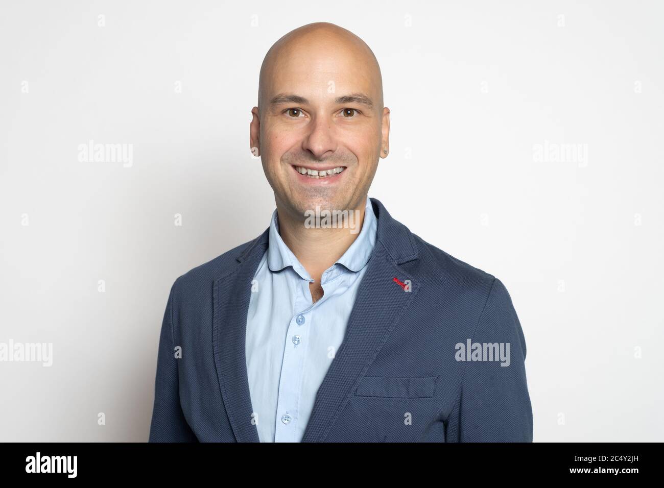 Un homme chauve en veste, confiant et charmant, sourit pendant que le mur du studio. Banque D'Images