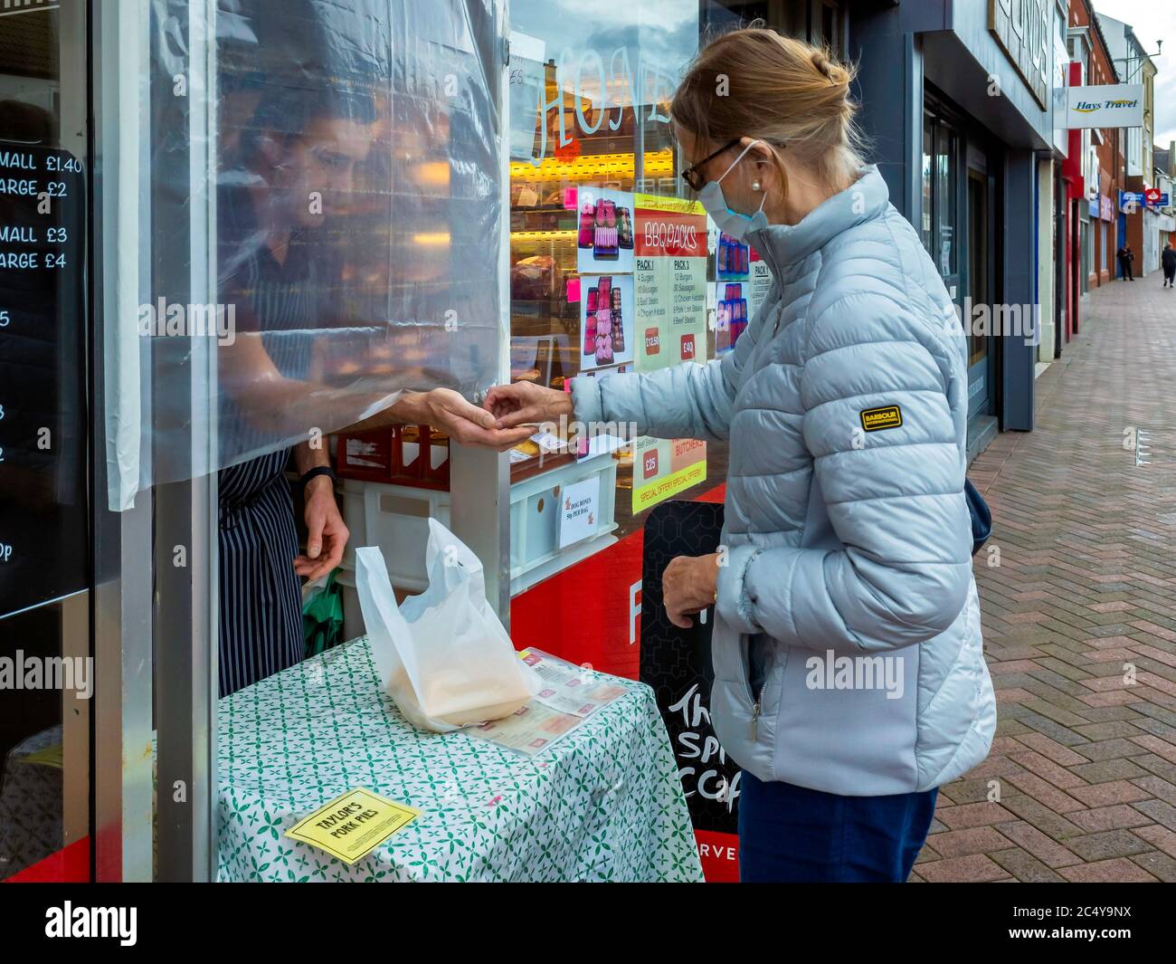 Une dame de premier plan achète un sandwich au bœuf chaud dans un boucherie, qui maintient une distance sociale en servant à une table à la porte d'entrée du magasin Banque D'Images