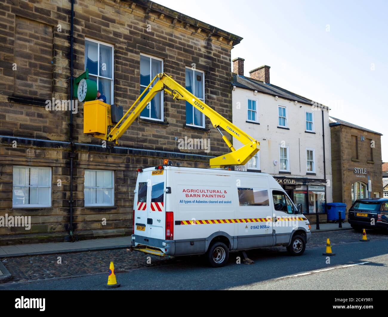 Homme sur un palan hydraulique effectuant une réparation de l'horloge sur la mairie de Stokesley North Yorkshire Banque D'Images