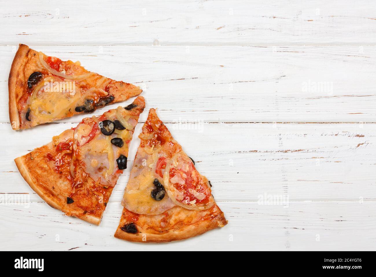 Vue de dessus des tranches de pizza avec tomates, olives noires, jambon et oignon sur une table en bois très près Banque D'Images