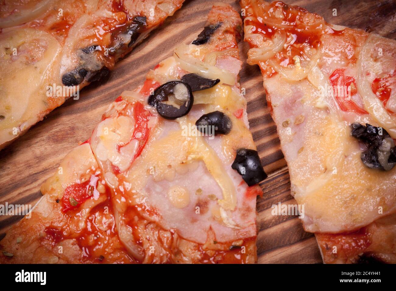Vue de dessus des tranches de pizza avec tomates, olives noires, jambon et oignon sur une table en bois très près Banque D'Images