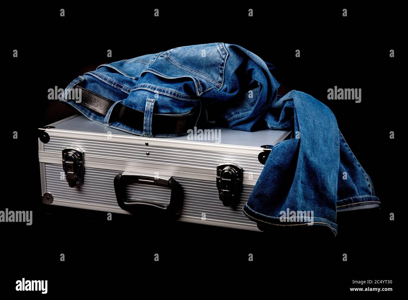 une paire de vieux jeans bleus reposant sur une valise en aluminium isolée sur le noir Banque D'Images