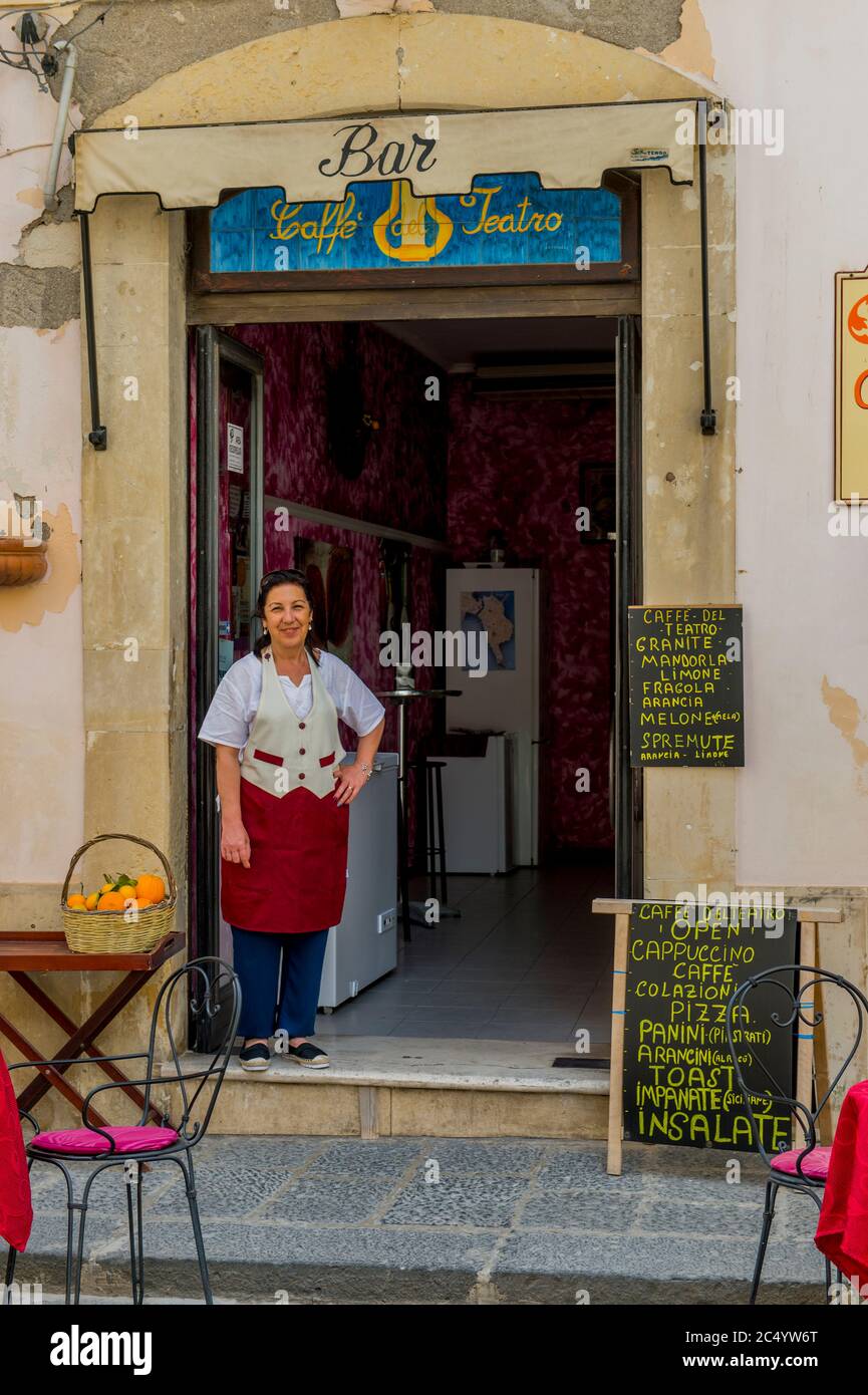 Scène de rue avec une femme chef debout devant son petit restaurant sur l'île d'Ortygia, la vieille ville de Syracuse sur l'île de Sicile, en Italie. Banque D'Images