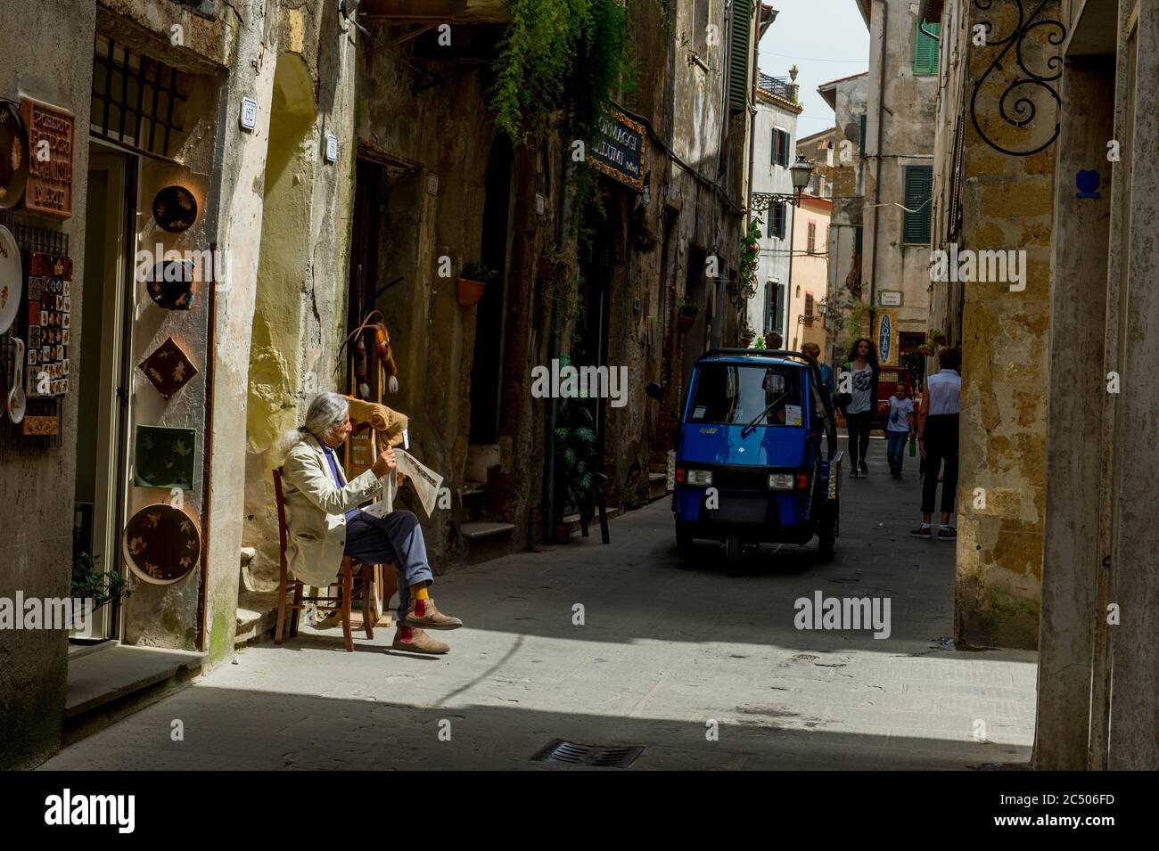 Scène de rue avec un homme lisant le journal et un Piaggio approchant, parfois appelé APE Piaggio, Apecar, APE car ou juste APE, qui est Banque D'Images