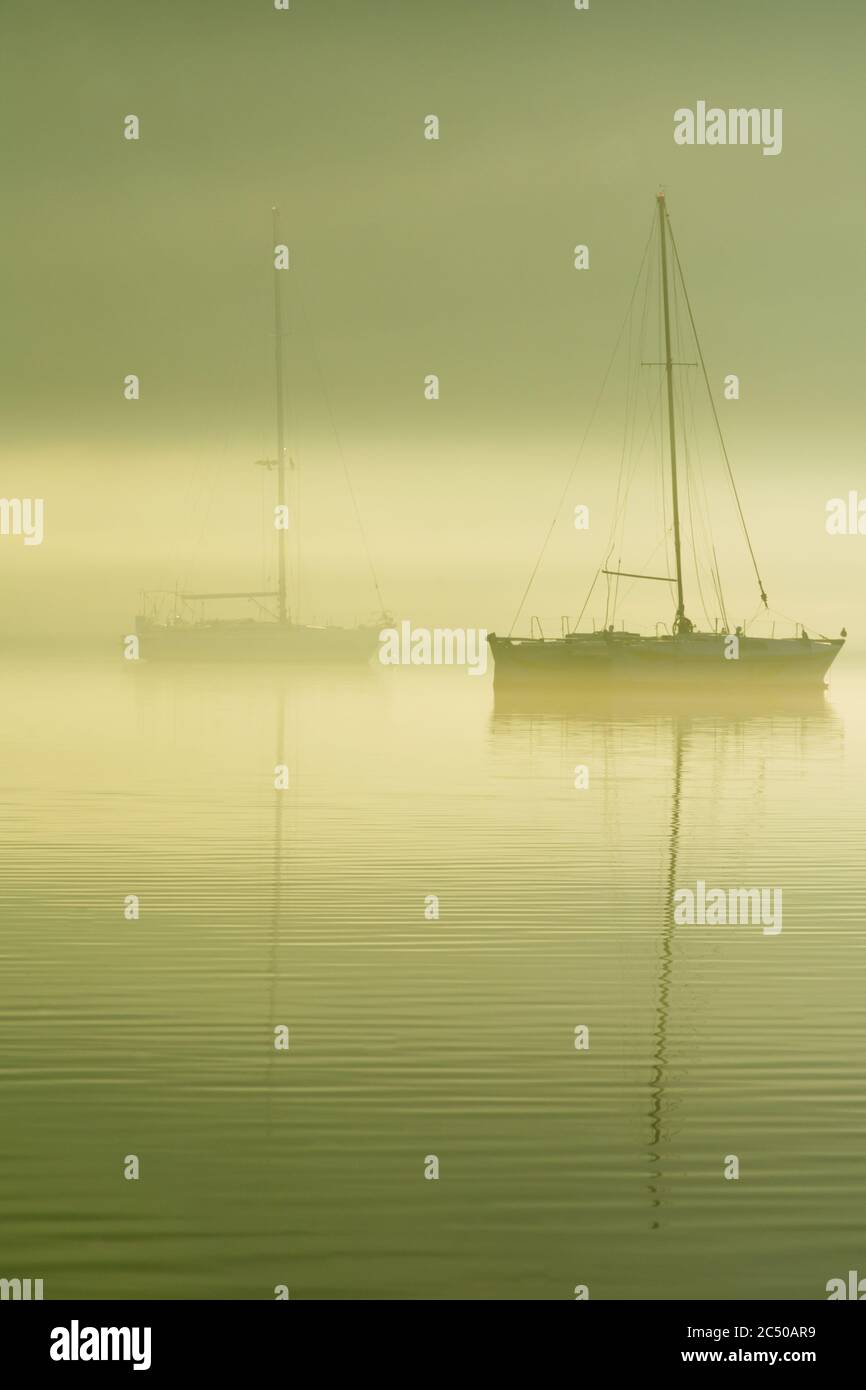 Des bateaux à voile amarrés dans la baie de Geni dans une matinée calme avec une forte brume et fumée sur la mer. Lefkada, Grèce. Banque D'Images