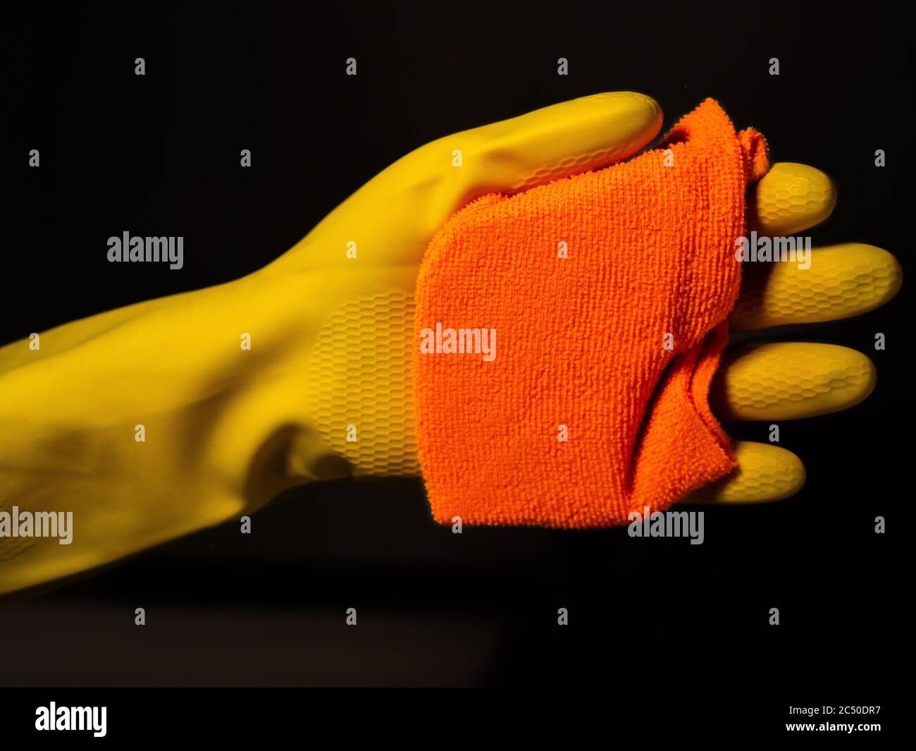 mains gantées jaunes avec un chiffon orange nettoyant un verre et un fond sombre Banque D'Images