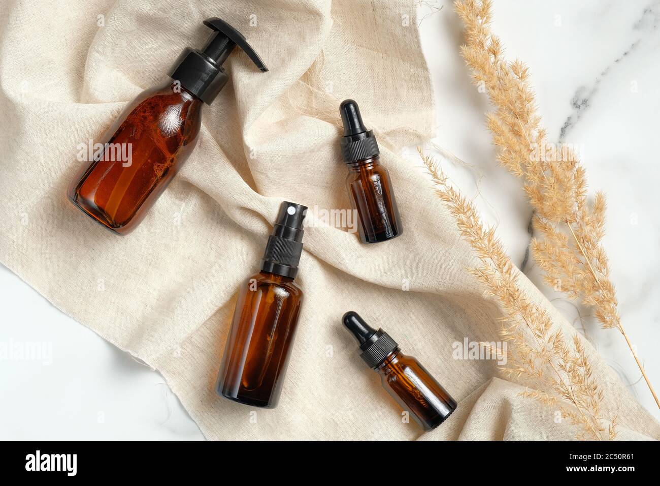 Collection de bouteilles en verre ambré avec tissu beige et fleurs sèches sur fond de marbre. Cosmétiques naturels biologiques, maquettes d'emballage. Banque D'Images