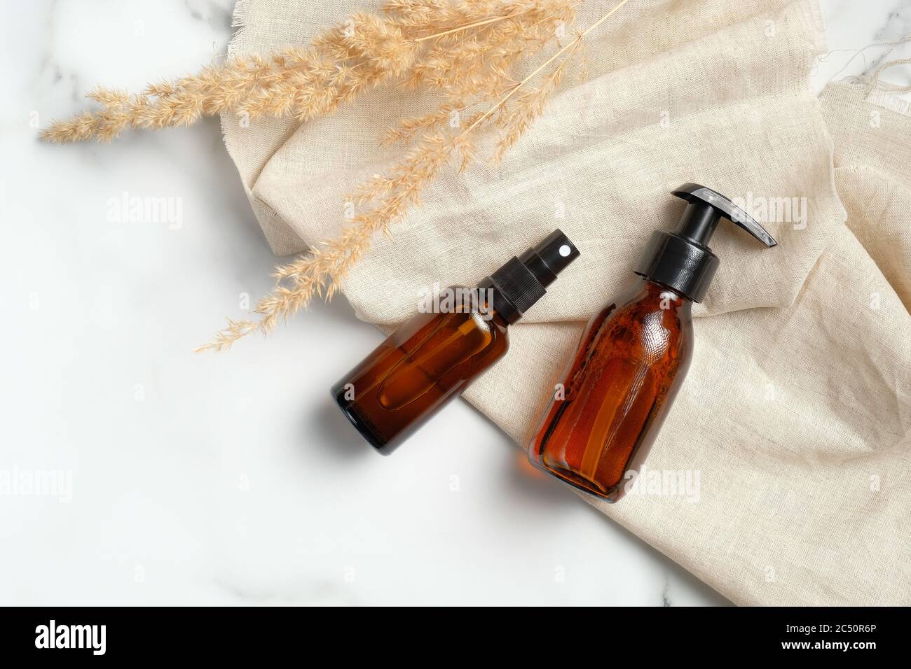 Ensemble de bouteilles en verre ambré foncé avec tissu beige et fleurs sèches sur fond de marbre. Luxe produits beauté emballages mockups, concept de soins de la peau. Banque D'Images