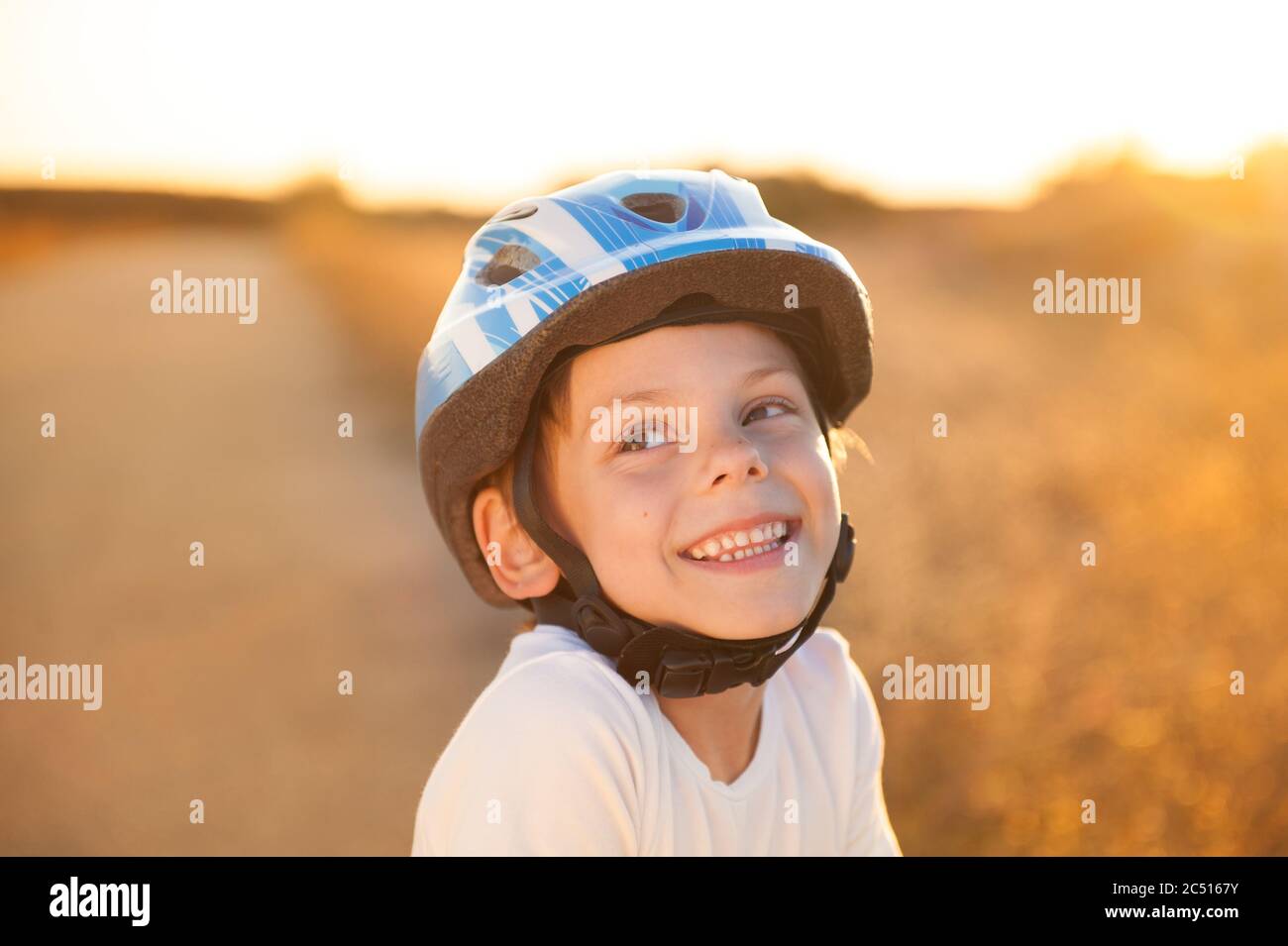 Portrait of happy smiling cute little caucasien enfant casque sport en bleu et chemise blanche sur l'été en plein air au coucher du soleil Banque D'Images