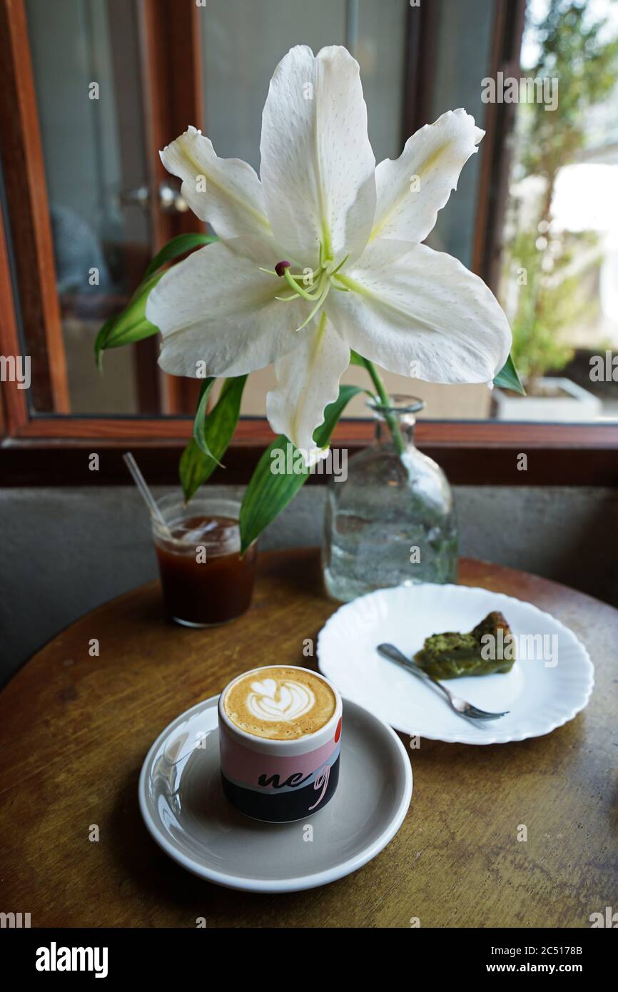 Tasse en céramique de Latte chaud, gâteau au thé vert Matcha, un verre de  Americano noir glacé sur une table en bois décorée de fleur de Lily Photo  Stock - Alamy