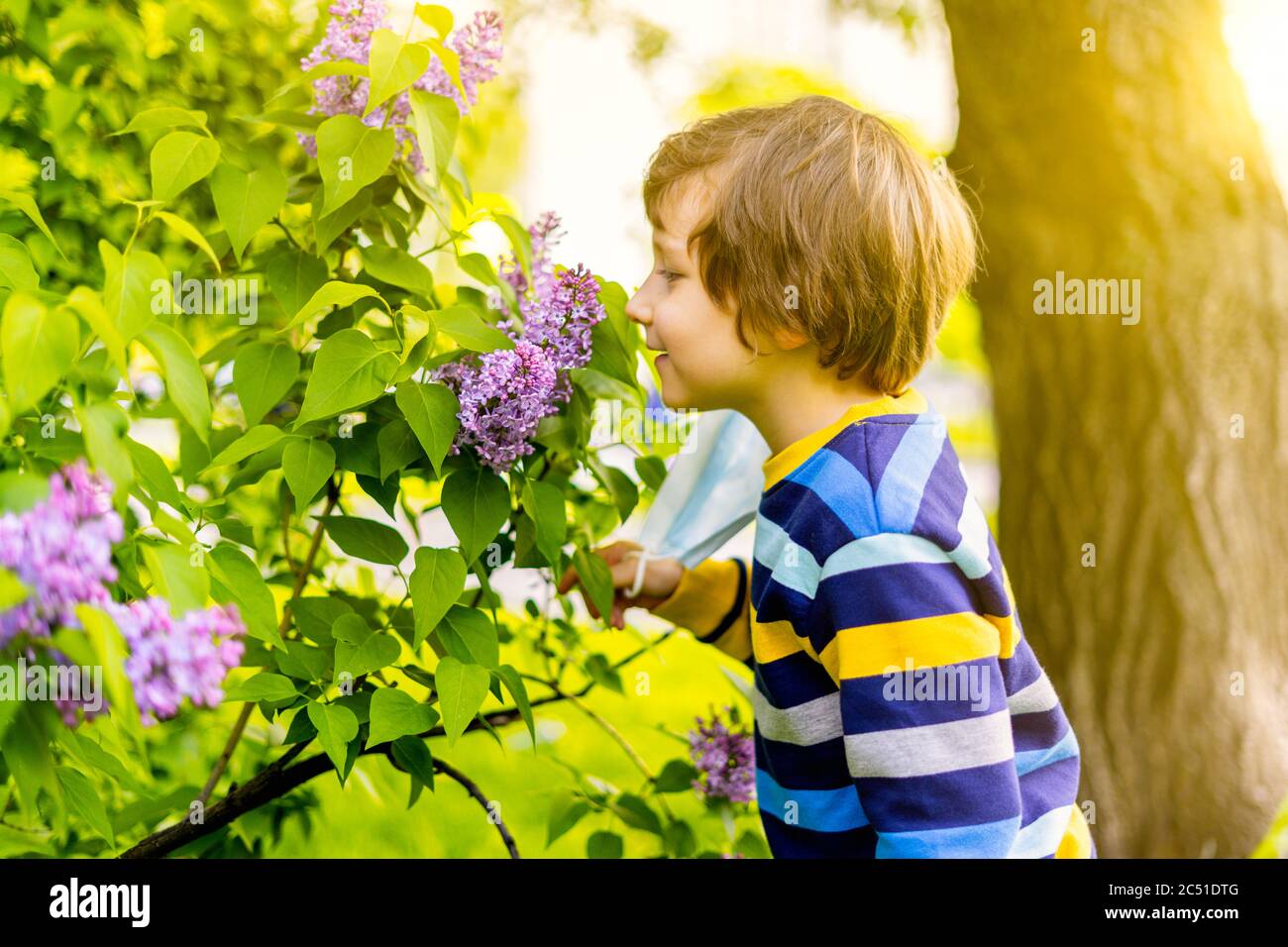 Joyeux garçon qui a pris son masque médical de protection et de l'air  respirable, sentant des fleurs de lilas. Joyeux enfant caucasien à la  journée ensoleillée à l'extérieur dans le parc Photo