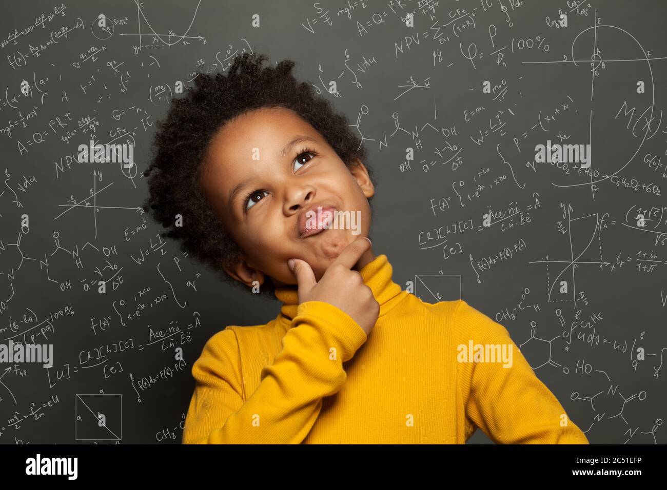 Enfant noir intelligent pensant sur fond de tableau noir avec des formules scientifiques Banque D'Images