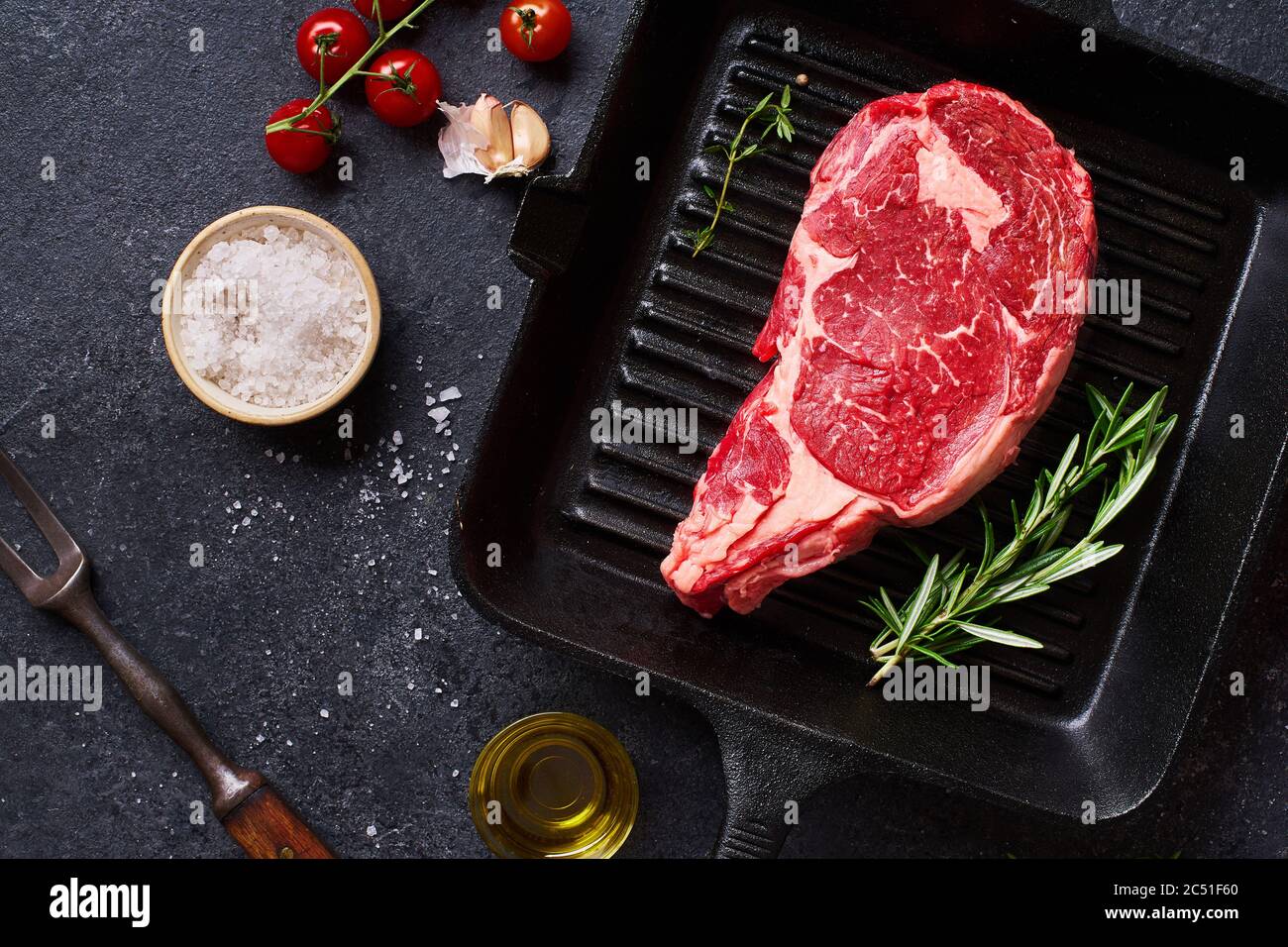 Vue du haut Black Angus, entrecôte de bœuf, steak d'oeil sur une poêle à  frire en fonte avec romarin frais, tomates cerises, huile d'olive et  épices. Mise en page créative W Photo