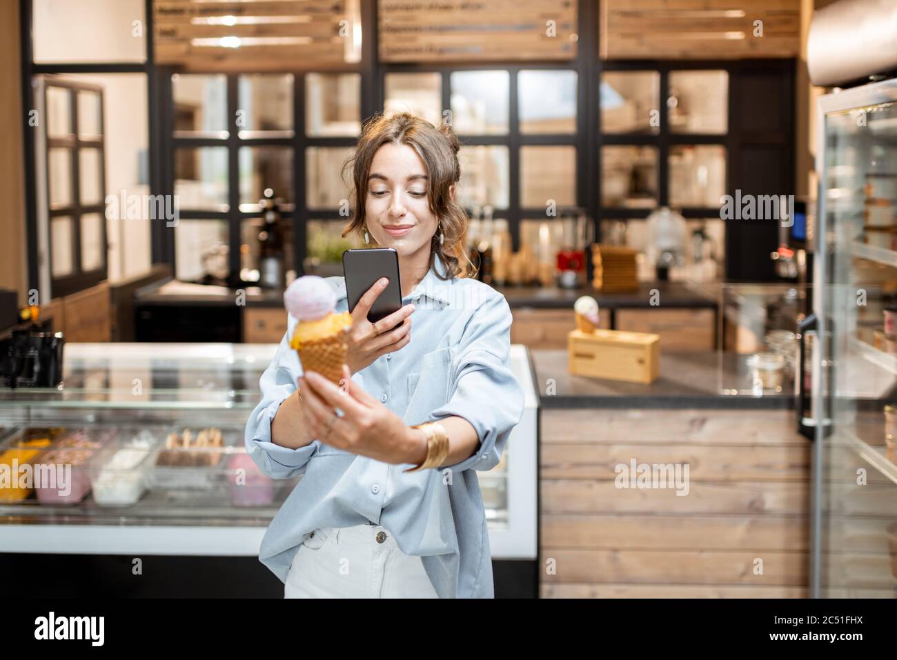 Jeune femme faisant une photo de glace délicieuse dans le cône de gaufres à l'intérieur. Acheter de la glace au magasin Banque D'Images