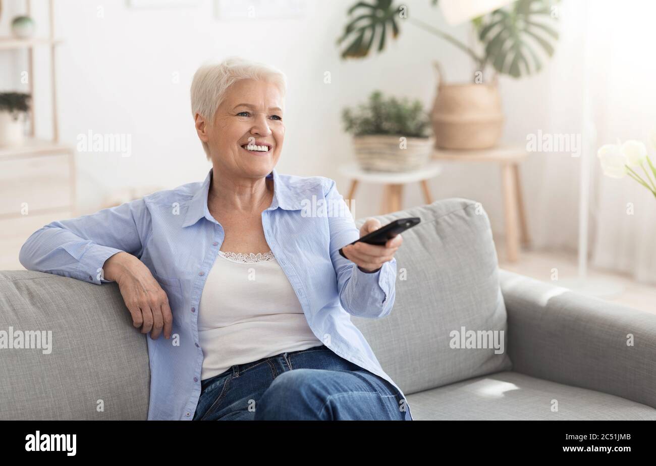 Bonne dame âgée regardant la télévision à la maison, assise sur un canapé avec contrôleur Banque D'Images
