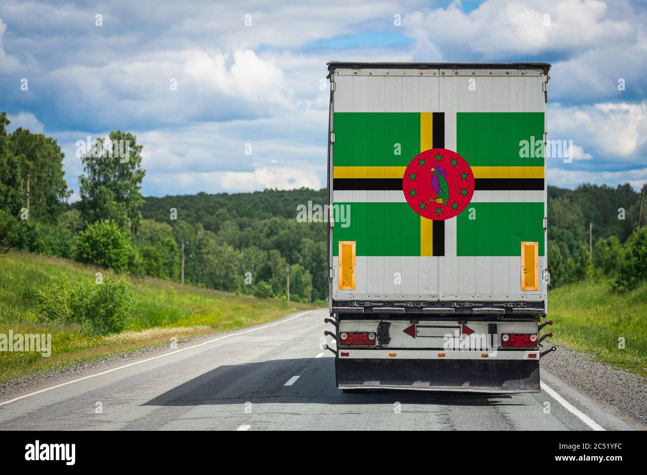 Un camion avec le drapeau national de la Dominique représenté sur la porte arrière transporte des marchandises vers un autre pays le long de la route. Concept d'exportation-importation,tr Banque D'Images