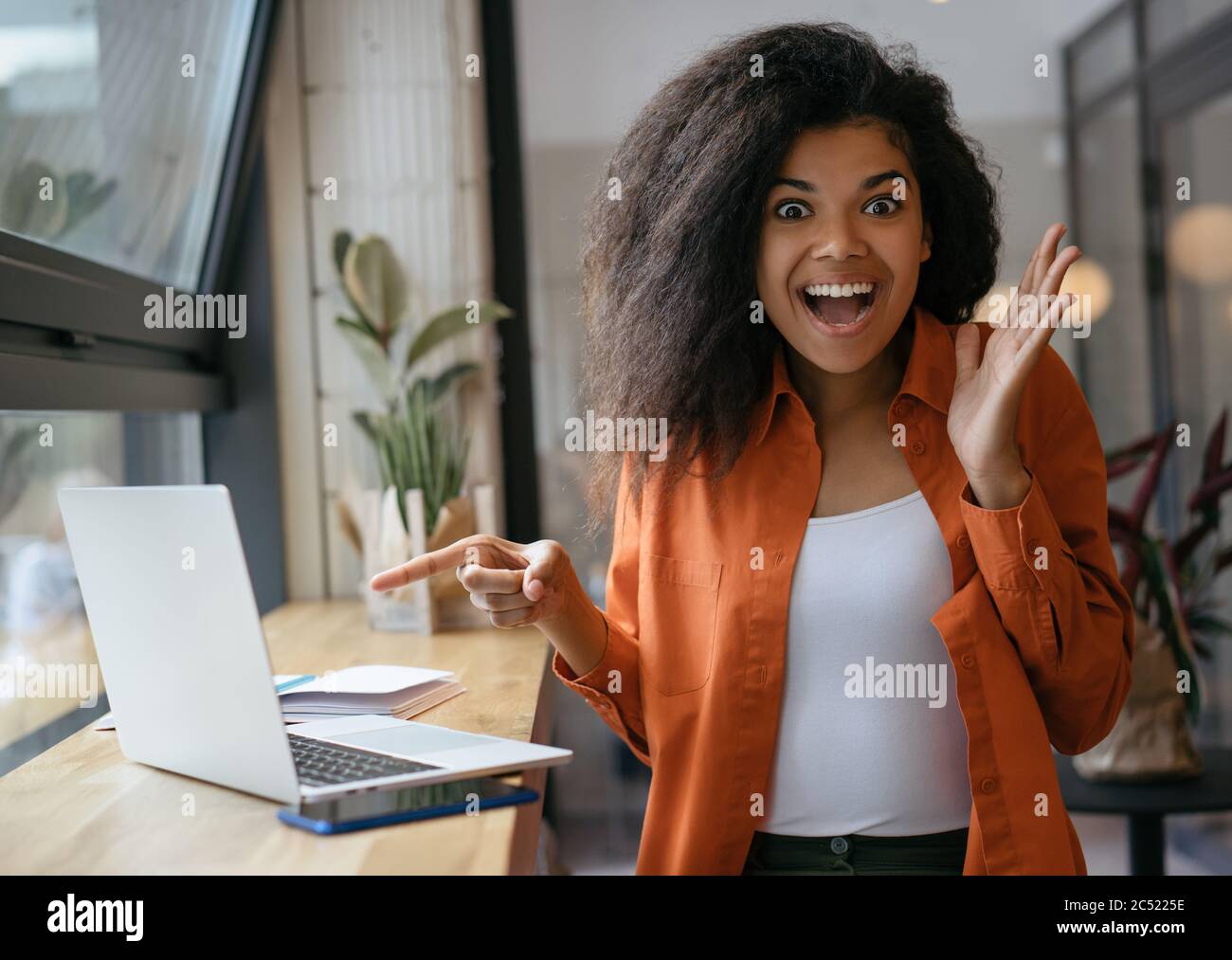 Une femme afro-américaine excitée pointant du doigt sur l'écran d'un ordinateur portable. Emotional hipster shopping en ligne avec des ventes de rabais, de l'argent de retour Banque D'Images