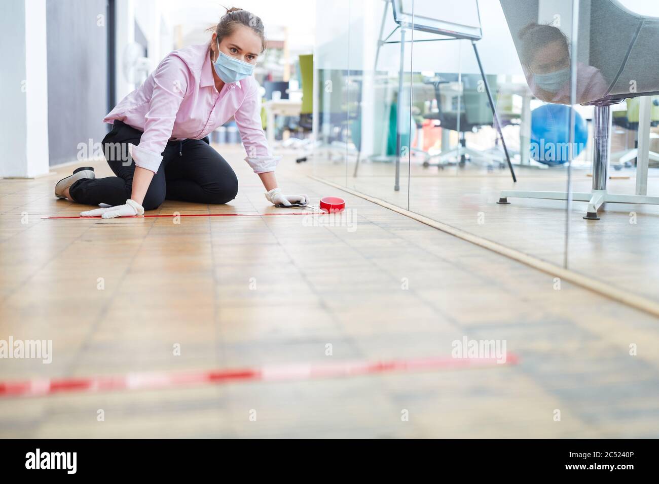 La femme d'affaires marque le sol du bureau avec du ruban adhésif pour garder la distance comme mesure de contrôle des infections Banque D'Images