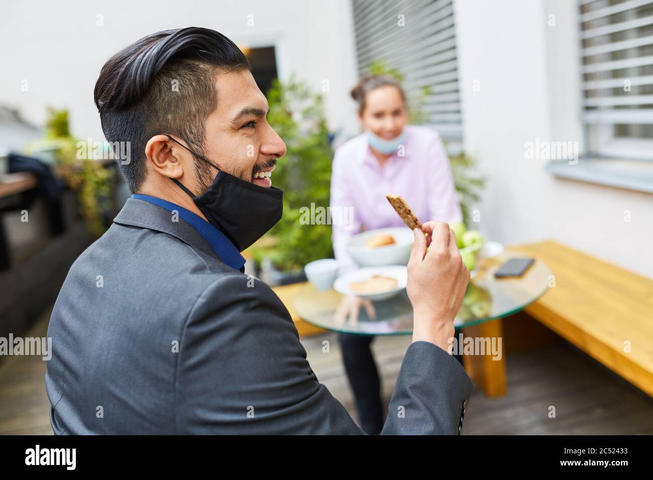 Homme d'affaires avec masque facial sur le menton ayant un snack dans un café pendant la pause déjeuner Banque D'Images