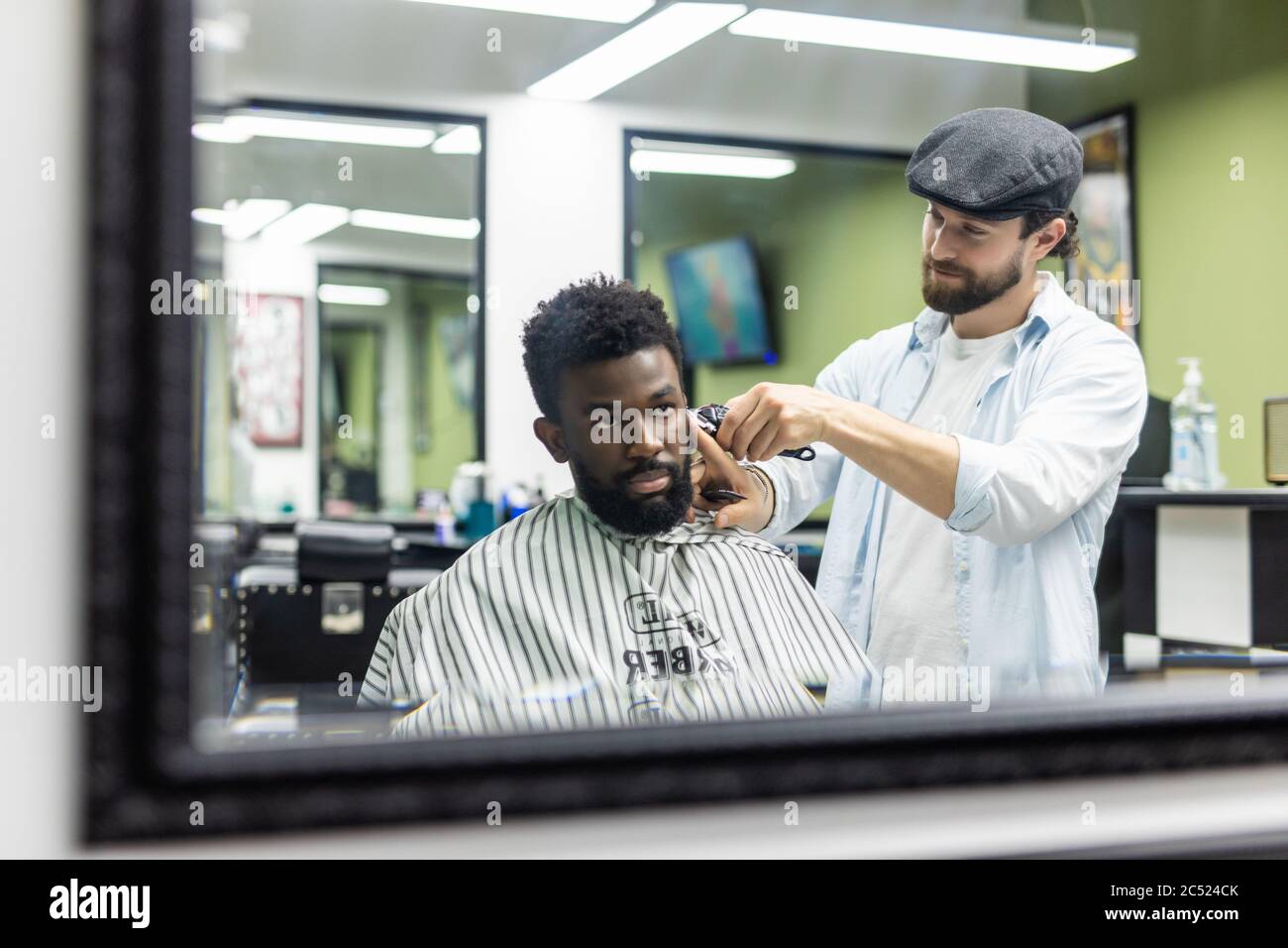 Jeune homme noir heureux en train d'être tondu avec une tondeuse électrique dans un salon de coiffure. Concept de soins de beauté pour hommes. Jeune homme africain souriant, qui devient nouveau Banque D'Images