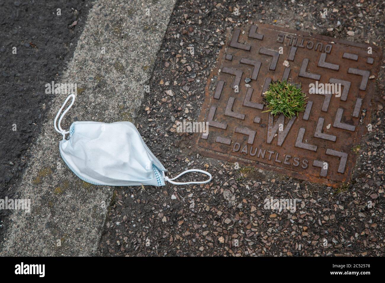 Masque de coronavirus jeté dans la rue à côté d'une couverture de drain sans dayte Banque D'Images
