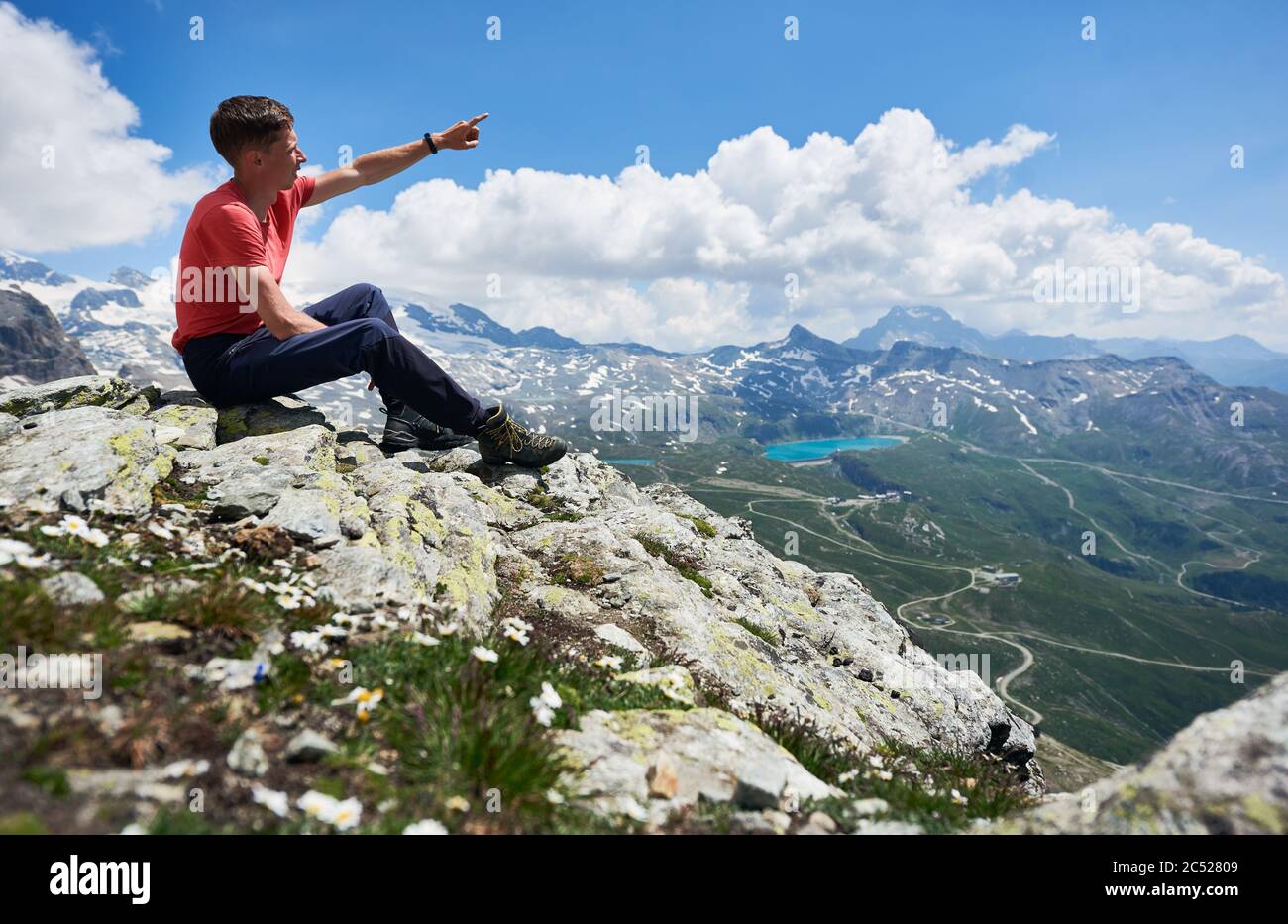 Touriste dans un t-shirt regardant de beaux paysages de montagnes et  pointant avec le doigt. Homme atteignant le sommet, assis sur des pierres.  Nature sauvage avec vues magnifiques par beau temps d'été.