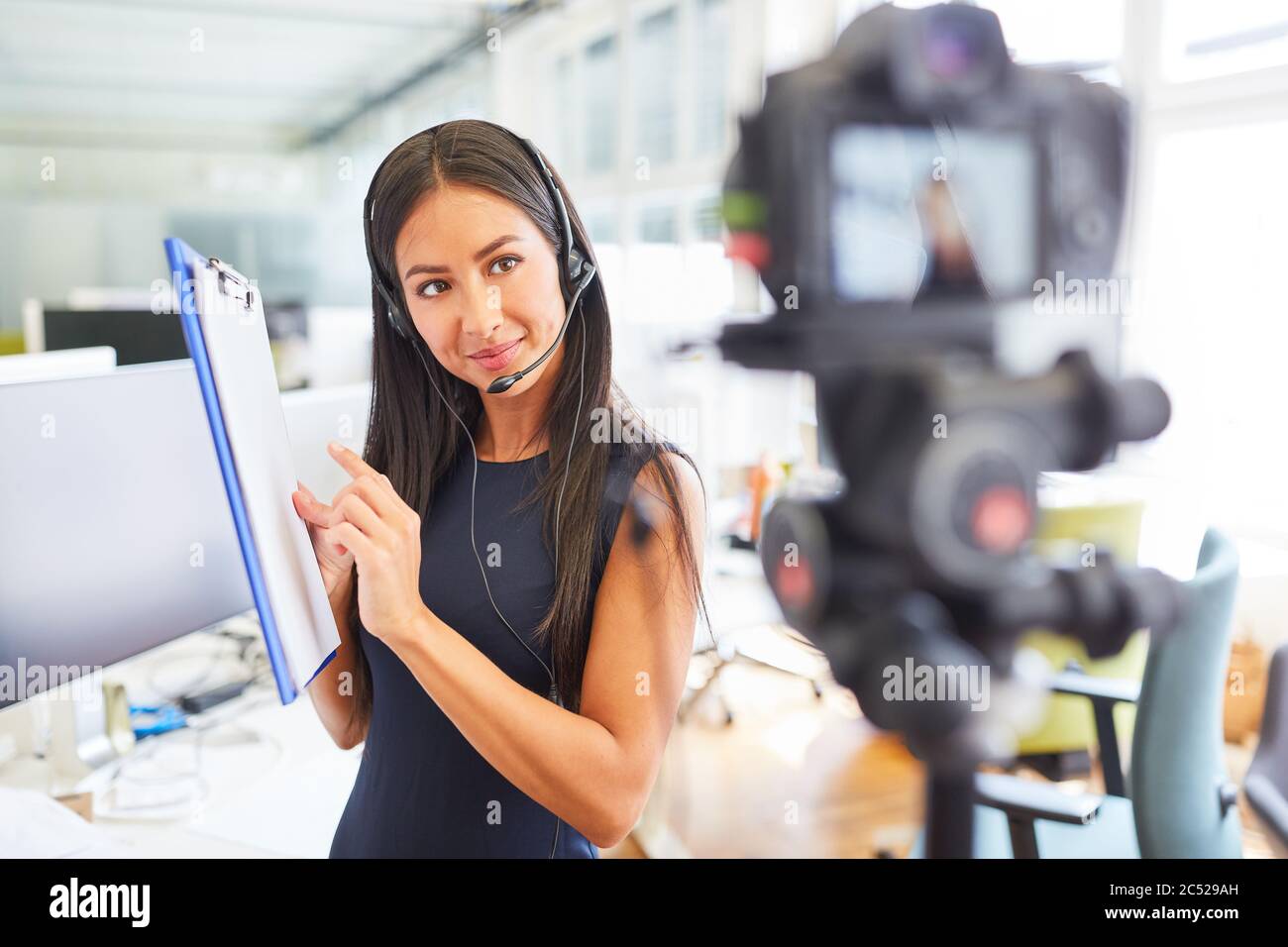 Une jeune femme d'affaires avec un presse-papiers et un casque produit un tutoriel vidéo Banque D'Images