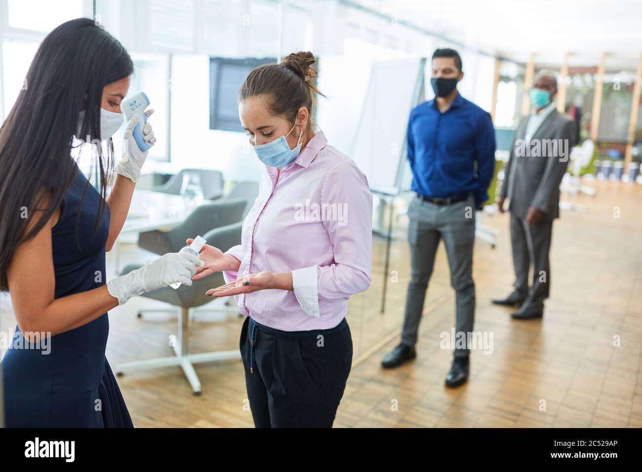 Les gens d'affaires se désinfectant les mains et mesurant la fièvre devant le bureau comme protection en raison de Covid-19 Banque D'Images Les gens d'affaires se désinfectant les mains et mesurant la fièvre devant le bureau comme protection en raison de Covid-19 Banque D'Images