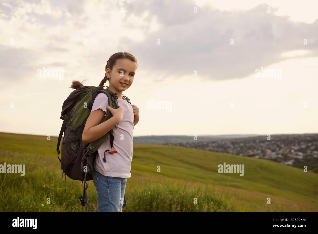Adorable petite fille avec sac à dos debout sur le dessus de montagne, espace de copie. Mignon enfant avec sac à dos randonnée dans la campagne Banque D'Images