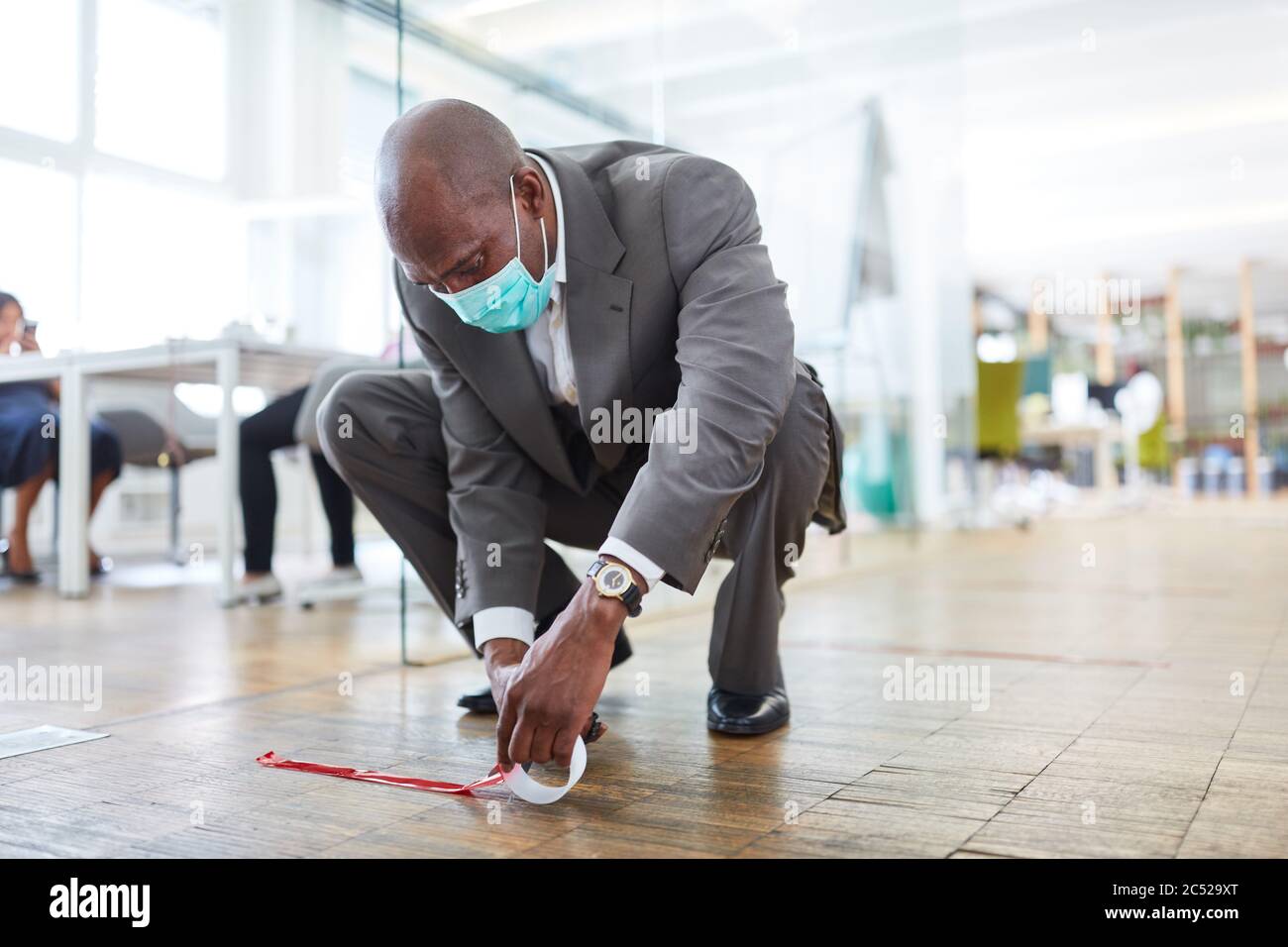 L'homme d'affaires africain marque le sol du bureau avec du ruban adhésif pour la distance en raison de Covid-19 Banque D'Images