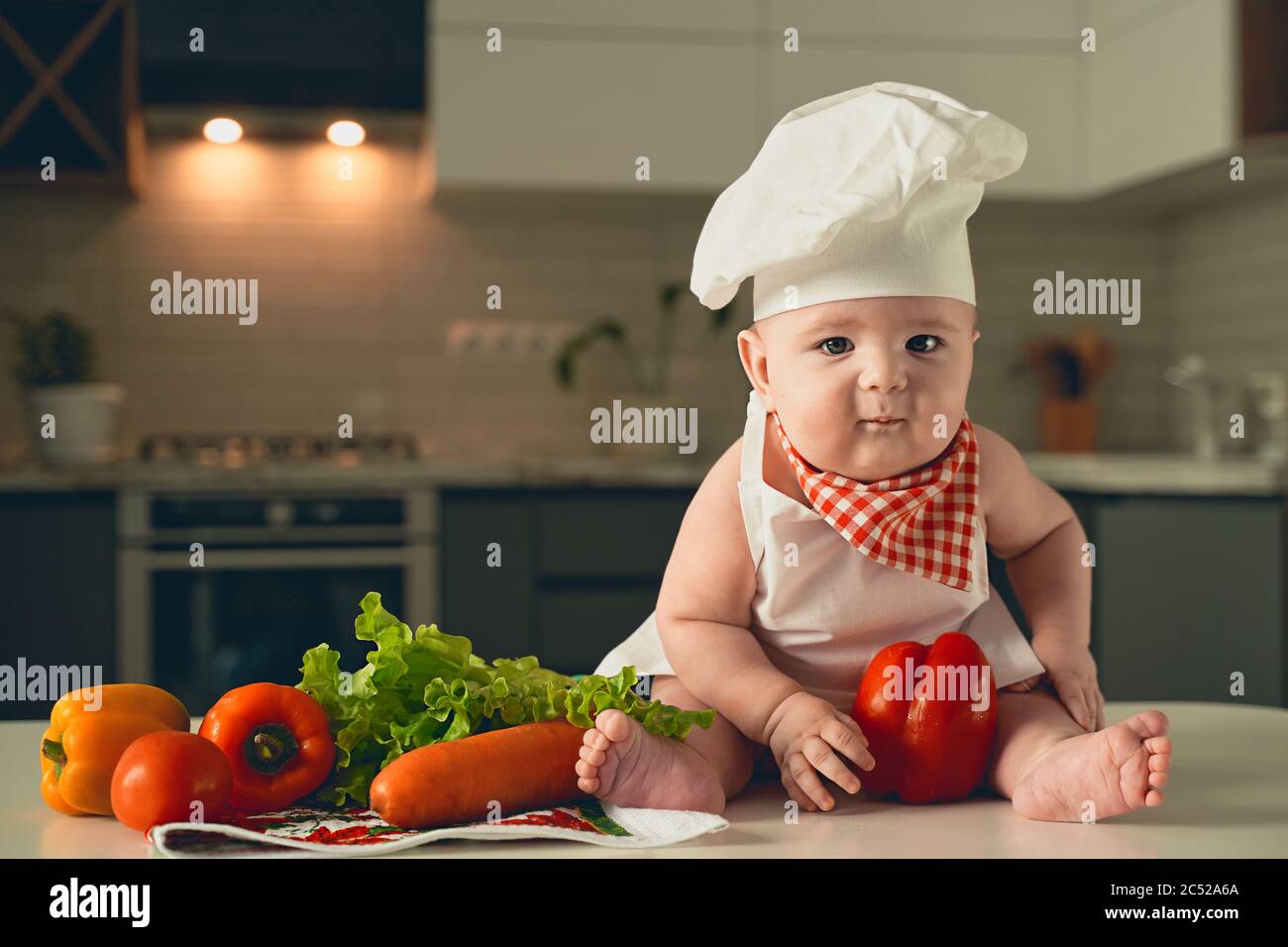 un petit enfant dans un chapeau de chef est assis à côté de légumes Banque D'Images