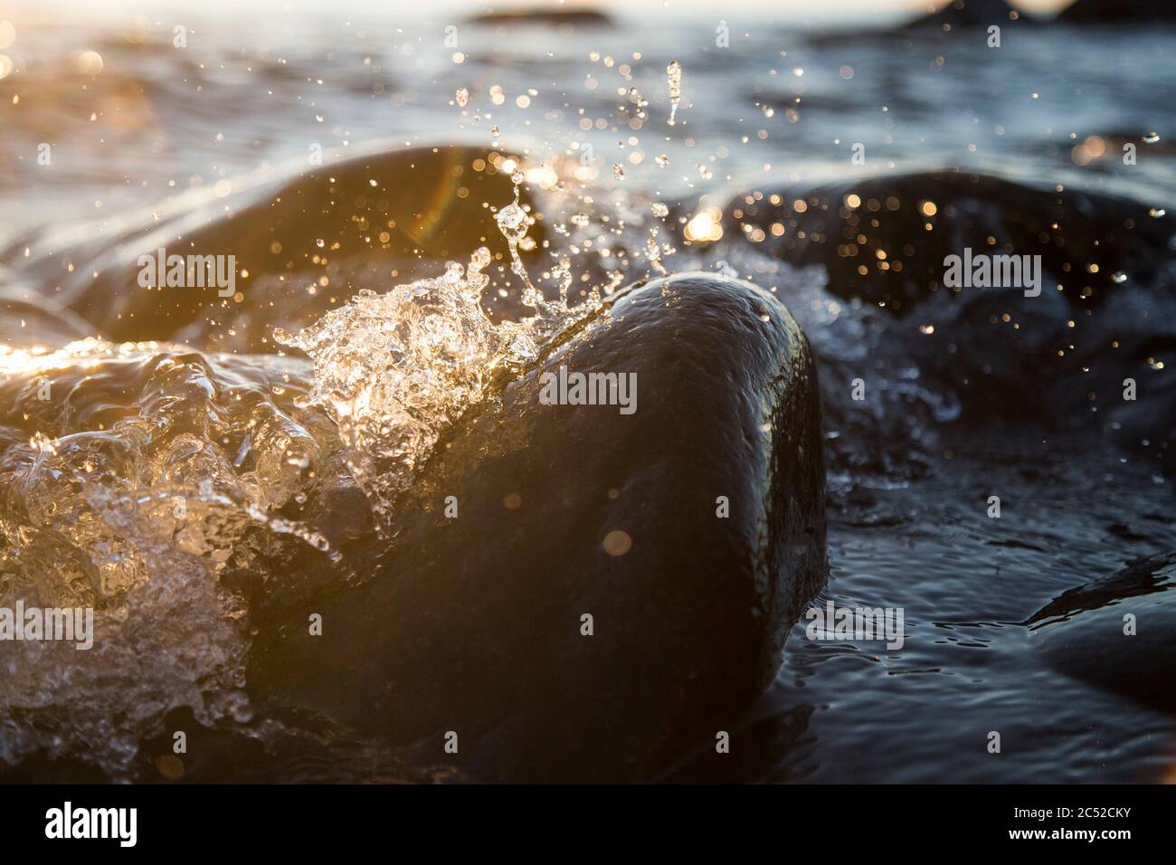 Gros plan photo des vagues de mer freinant sur une mer humide pierres soleil d'été, éclaboussures d'eau, rayons de soleil, réflexions sur les gouttes d'eau. Banque D'Images