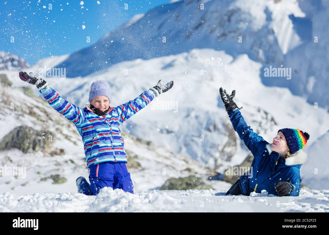 Deux jolies filles ont le plaisir de s'asseoir ensemble sur le sol jeter de la neige dans l'air sur la belle montagne Banque D'Images