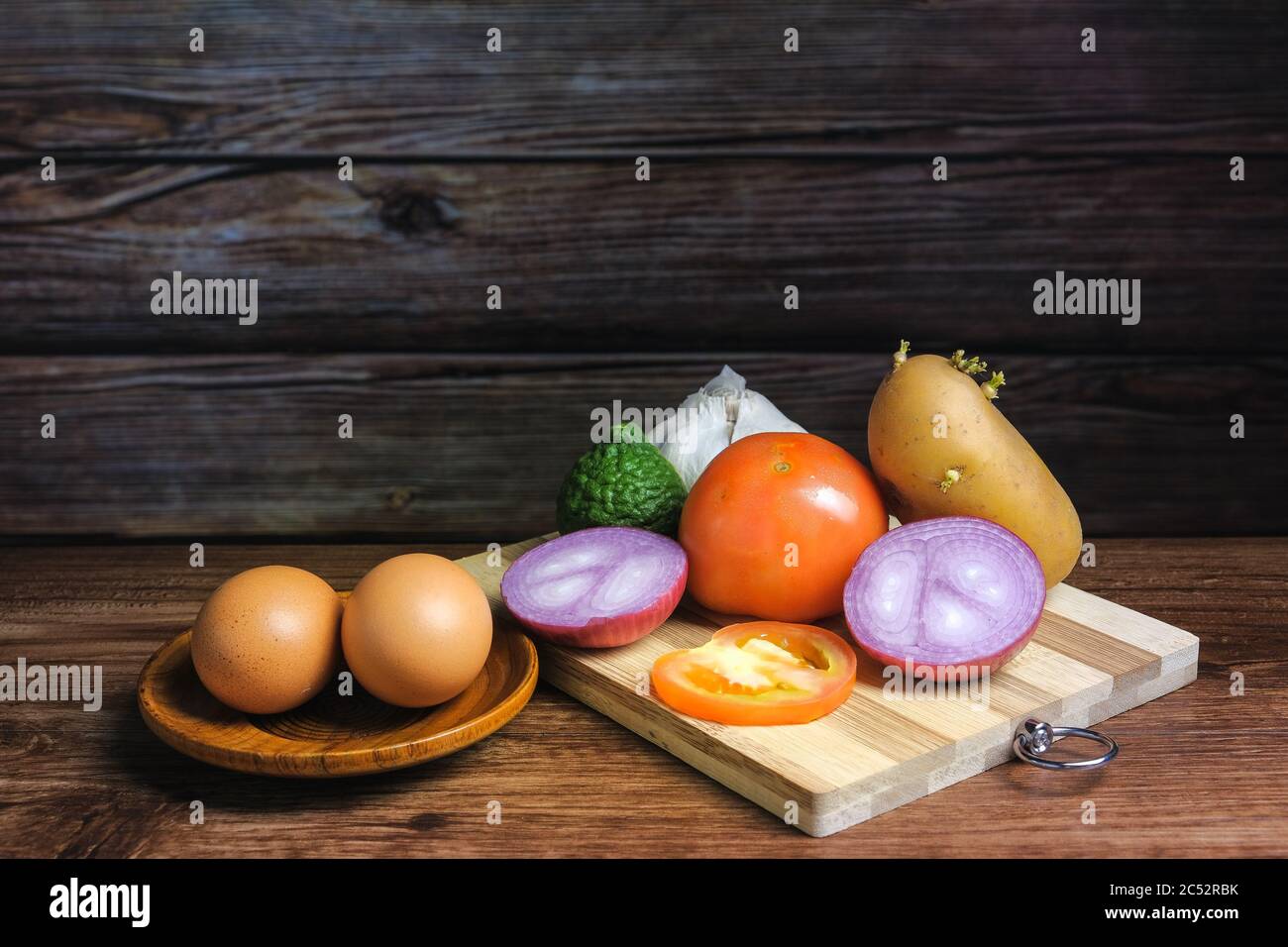 Tomate, ail, caille, oignon, oeufs et pomme de terre sur une planche à découper en bois Banque D'Images