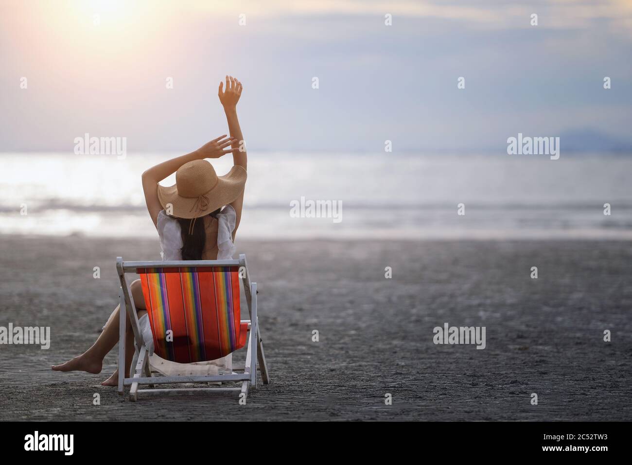 Vue arrière d'une femme assise dans une chaise longue sur la plage au coucher du soleil, Thaïlande Banque D'Images