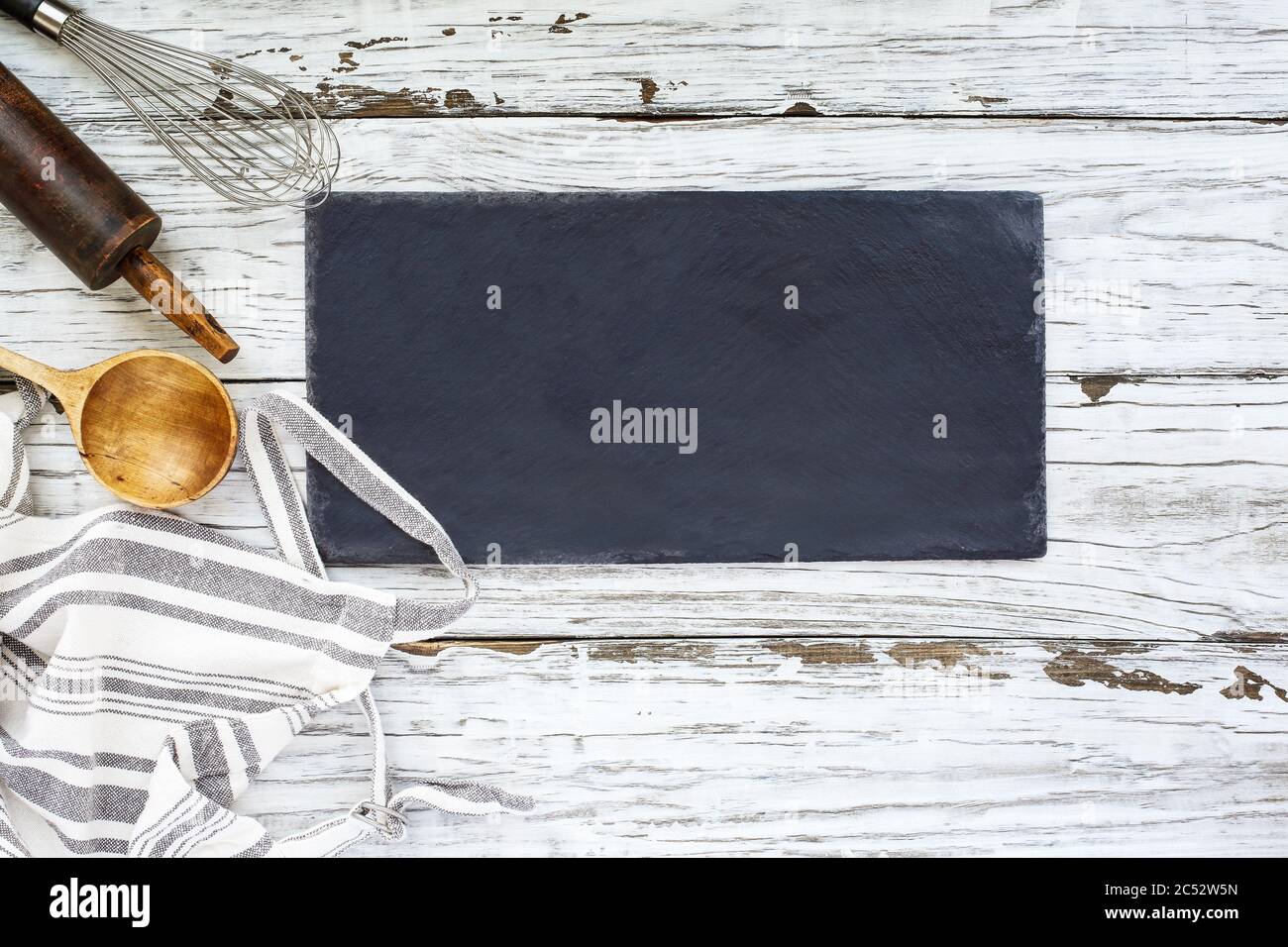 Affiche vierge avec fournitures de cuisson. Tablier, fouet, vieille cuillère en bois et broche de roulement antique sur fond de bois blanc ou table. Photo prise de la meilleure vie Banque D'Images