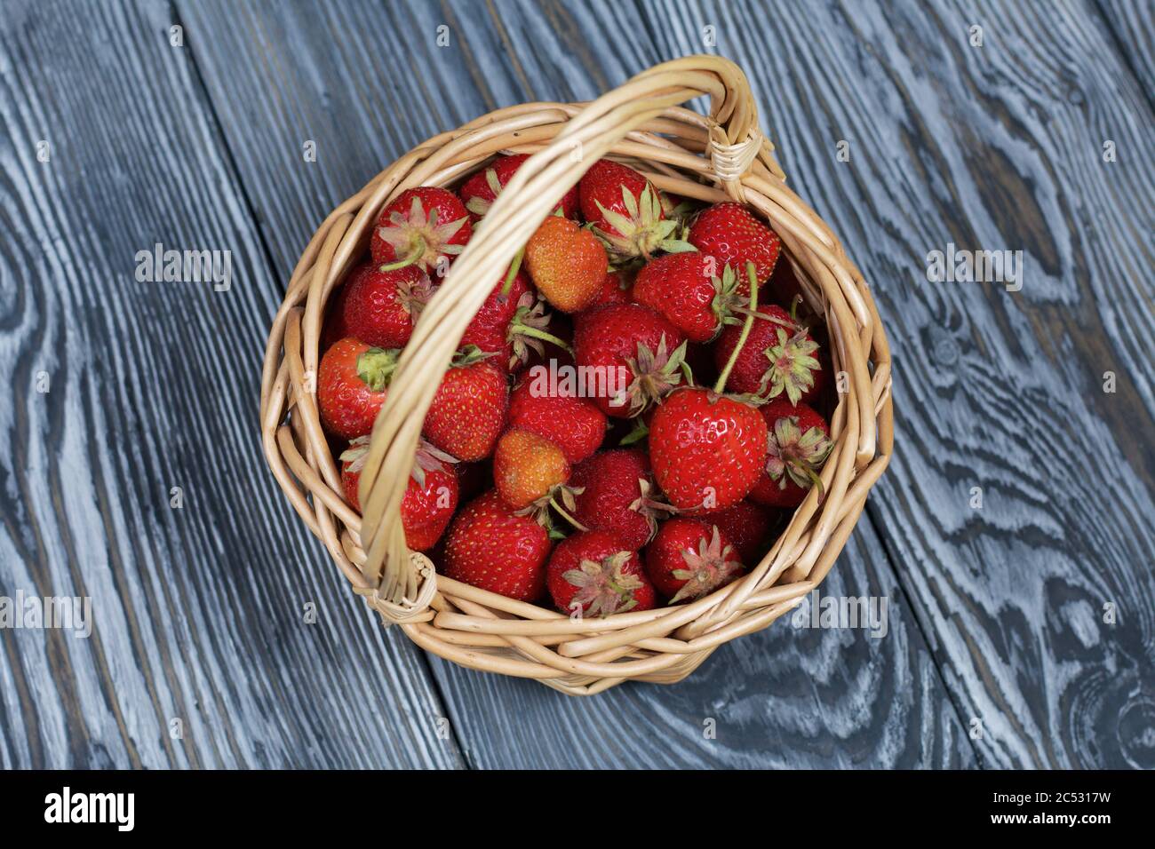 Fraises rouges mûres dans un panier en osier. Sur le fond des planches de pin peintes en blanc et noir. Récolte 2020. Vue d'en haut. Banque D'Images