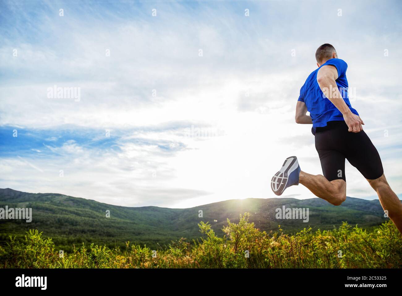 le coureur de fond de l'athlète courir la prairie de montagne en rayons de coucher de soleil Banque D'Images