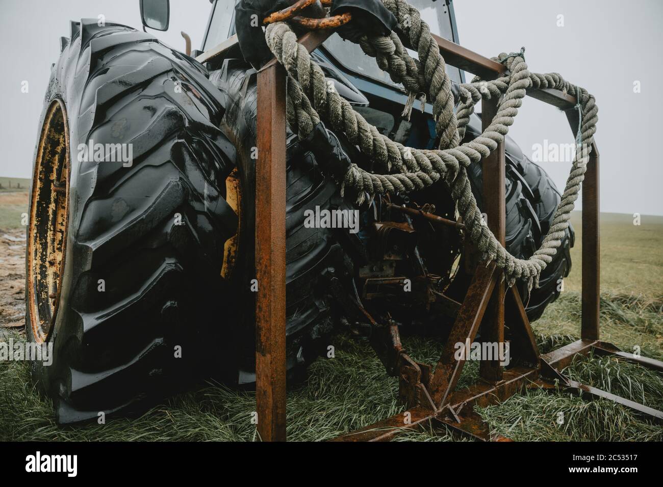 Détail de l'épaisse corde humide enroulée et suspendue sur le châssis rouillé arrière sur la partie arrière d'un vieux tracteur abandonné avec d'énormes roues doubles Banque D'Images