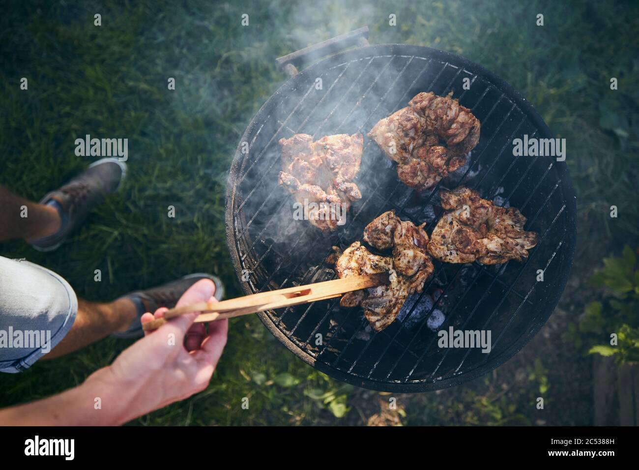 Jeune homme qui a grillé de la viande de poulet sur le barbecue dans le jardin pendant la journée d'été. Banque D'Images
